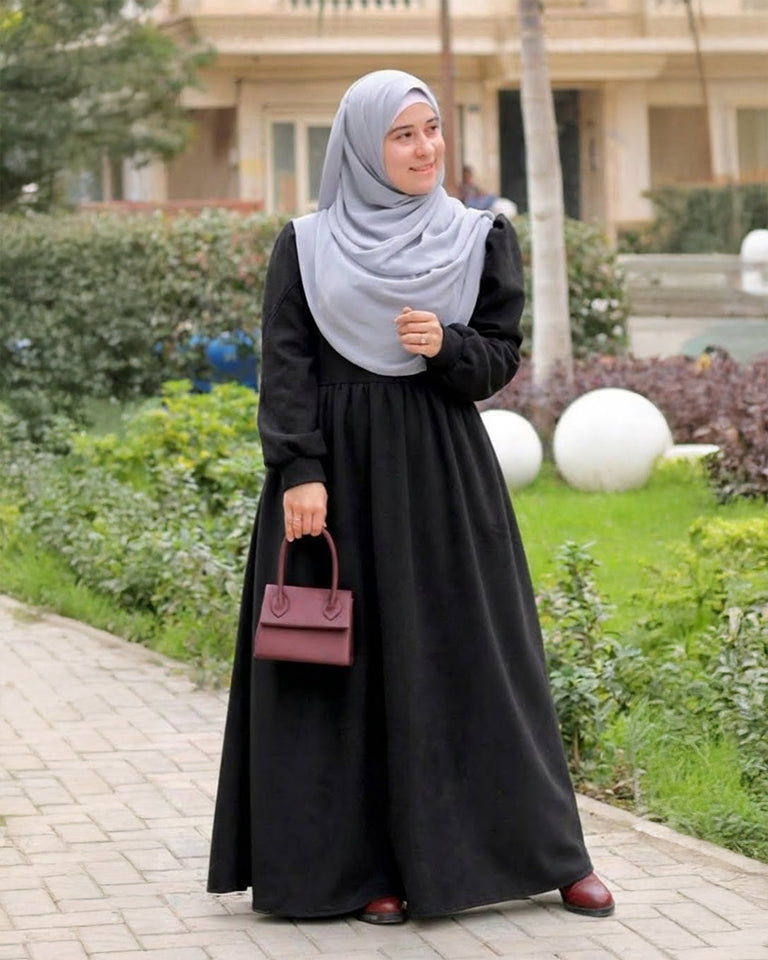 مودل ترتدي فستان طويل مودست باللون اسود من ضي Dhai، تصميم واسع ومحتشم بأكمام طويلة مع حجاب مطابق، إطلالة أنيقة وبسيطة على خلفية بيضاء.
فستان برجاندي 
مودست فاشون
دريس ميلتون
دريس ملتون