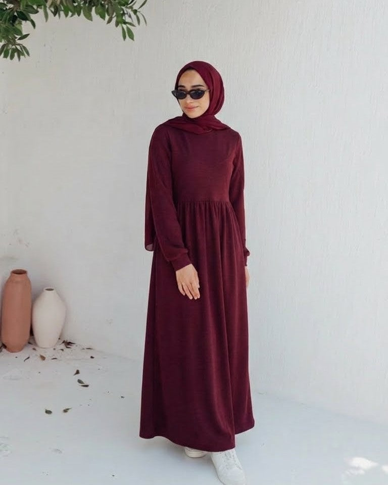 مودل ترتدي فستان طويل مودست باللون العنابي من ضي Dhai، تصميم واسع ومحتشم بأكمام طويلة مع حجاب مطابق، إطلالة أنيقة وبسيطة على خلفية بيضاء.
فستان برجاندي 
مودست فاشون
