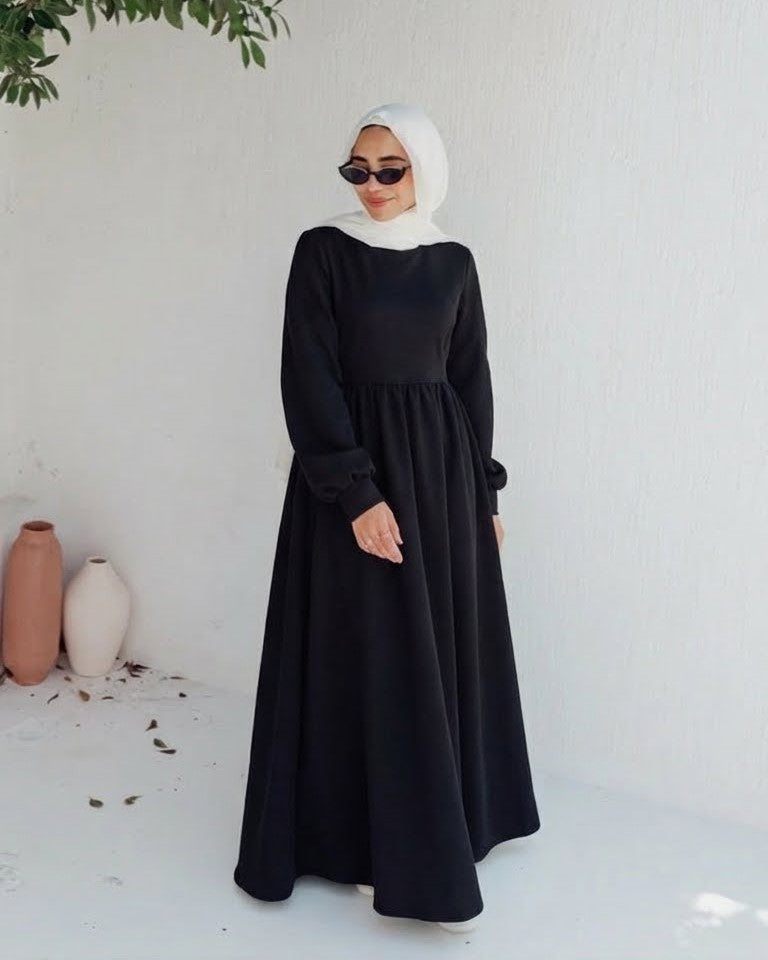 مودل ترتدي فستان طويل مودست باللون اسود من ضي Dhai، تصميم واسع ومحتشم بأكمام طويلة مع حجاب مطابق، إطلالة أنيقة وبسيطة على خلفية بيضاء.
فستان برجاندي 
مودست فاشون
دريس ميلتون
دريس ملتون